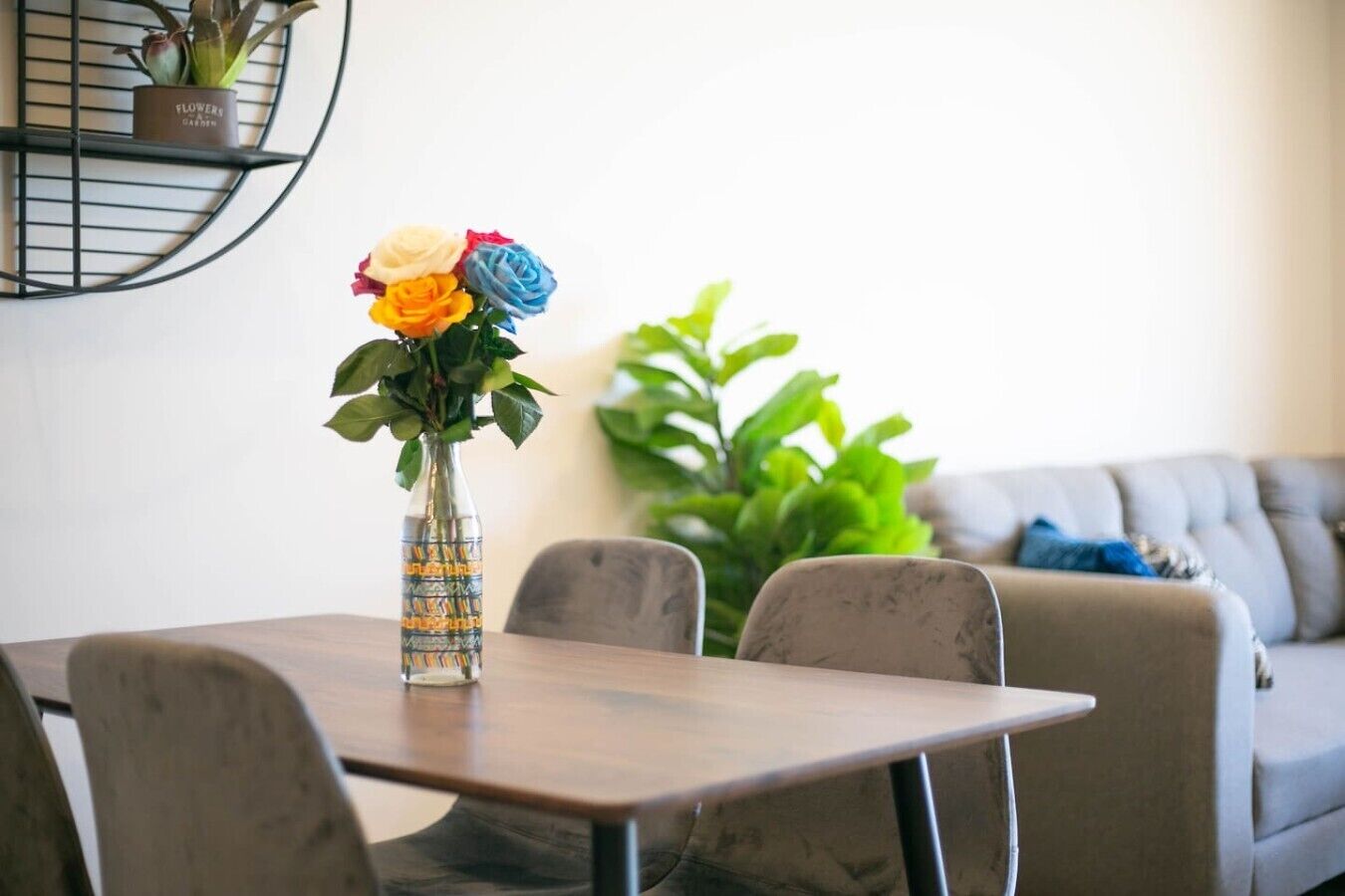 A dining table with chairs, a vase with flowers, and a sofa in the background.