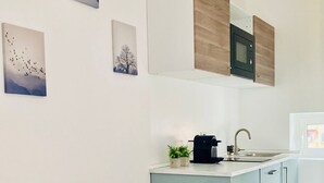 Una cocina moderna con una isla central, armarios blancos y un microondas. Hay dos cuadros en la pared, un lavamanos con grifo y una planta pequeña en la isla.