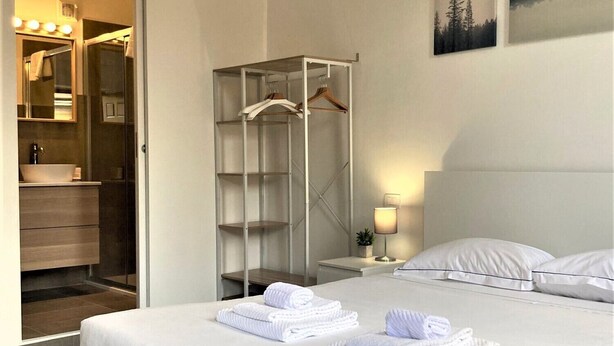 Una habitación de hotel moderna con una cama grande, un vestidor amplio y un baño con tocador y espejo.