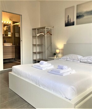 Ein modernes Hotelzimmer mit einem großen Bett, einem begehbaren Kleiderschrank und einem Badezimmer mit Waschtisch und Spiegel.