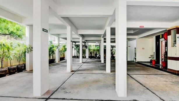 Un espacio al aire libre cubierto con pilares blancos, suelo de hormigón y plantas en macetas.