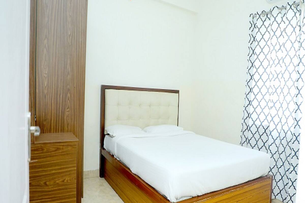 A single bed in a room with a wooden headboard, a wooden wardrobe, and a patterned curtain.