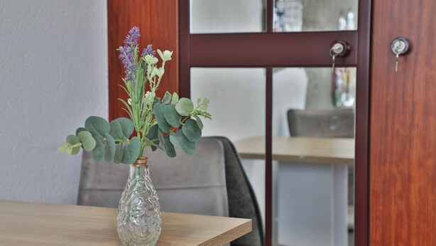 Visão clara de uma mesa de madeira com um vaso de vidro contendo flores verdes e roxas.