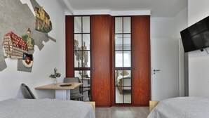 Quarto de hotel com duas camas, uma escrivaninha, uma cadeira, televisão e guarda-roupa com espelho.