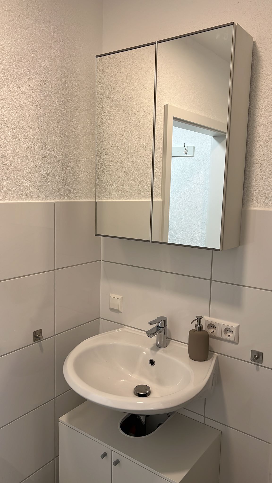 A bathroom with a white sink, a mirror above it, and a cabinet below.