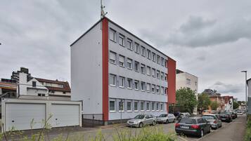 Ein mehrstöckiges Gebäude mit flachem Dach, großen Fenstern und einem roten Akzent an der Ecke.