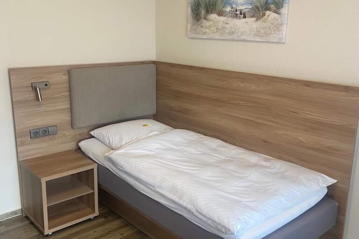 Un dormitorio compacto con una cama individual, una mesita de noche de madera y un cuadro colgado en la pared.
