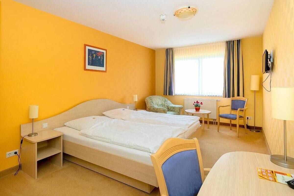 Habitación de hotel con cama, mesitas de noche, escritorio, silla, televisor y ventana con cortinas.