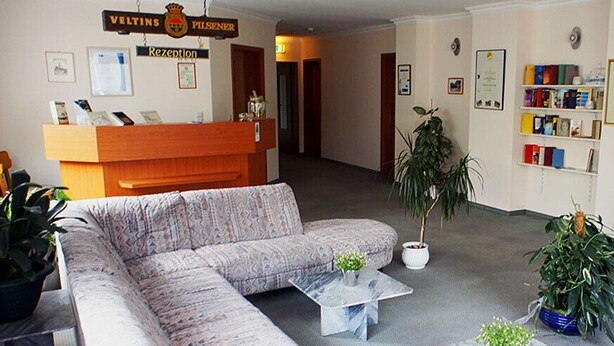 A reception area with a reception desk, a sofa, a coffee table, and several potted plants. - Hotel am Stern (Uelzen)