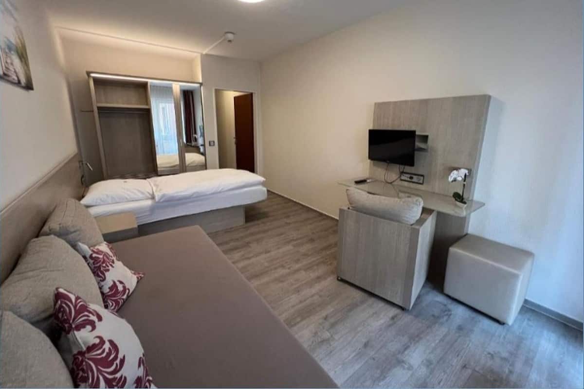 Una habitación de hotel moderna con cama, sofá, televisor y un pequeño rincón de descanso.