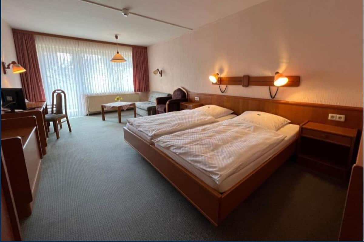 Habitación de hotel con dos camas, un escritorio, una silla, una lámpara y una ventana con cortinas.