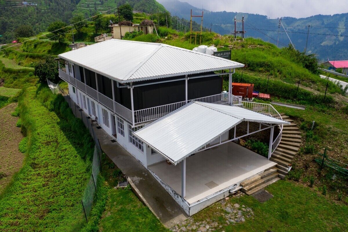 A two-story building with a flat roof and a covered porch, surrounded by lush green hills.