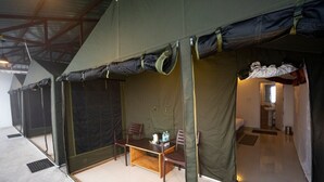 Une pièce aménagée sous une tente, avec une table et des chaises, un petit coin cuisine et une salle de bain visible depuis l’entrée de la tente.