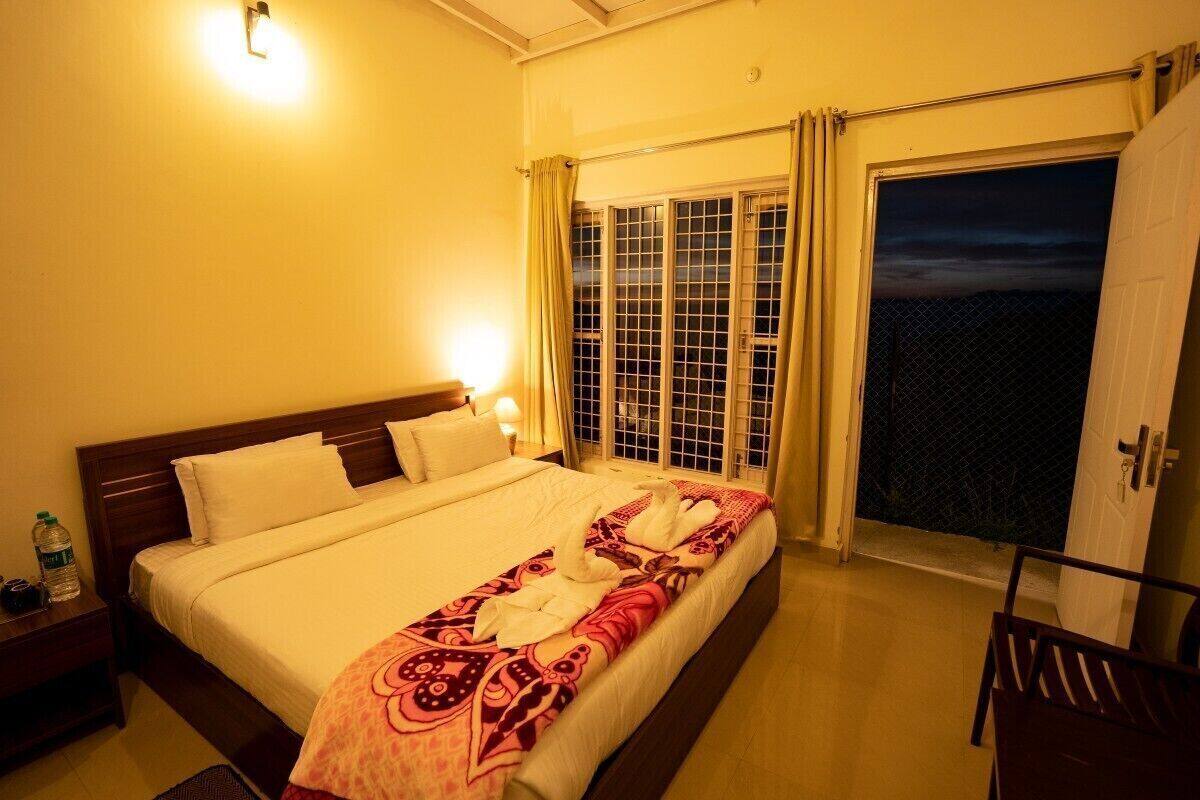 A hotel room with a bed, a nightstand, a chair, and a view through a window with curtains.