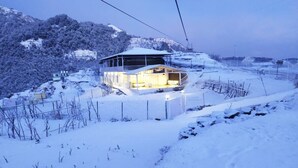 Une montagne enneigée, surmontée d’un bâtiment illuminé, probablement un hôtel, d’où l’on a une vue dégagée sur le paysage enneigé environnant.