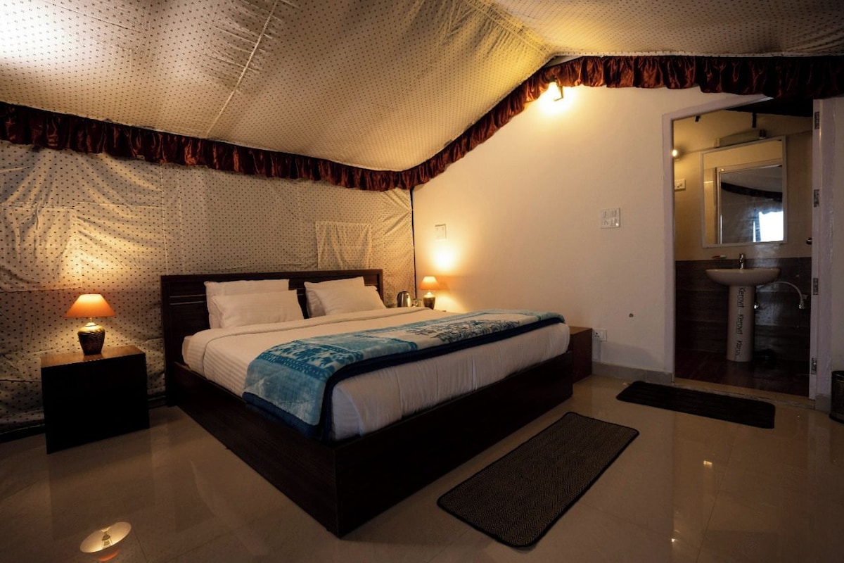 A bedroom with a large bed, two bedside lamps, a nightstand, a bathroom with a sink and mirror, and a ceiling with a patterned design.