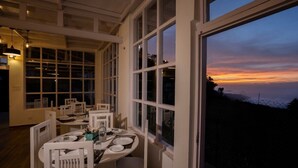 Un espace repas avec des meubles blancs et de grandes fenêtres donnant sur un coucher de soleil.