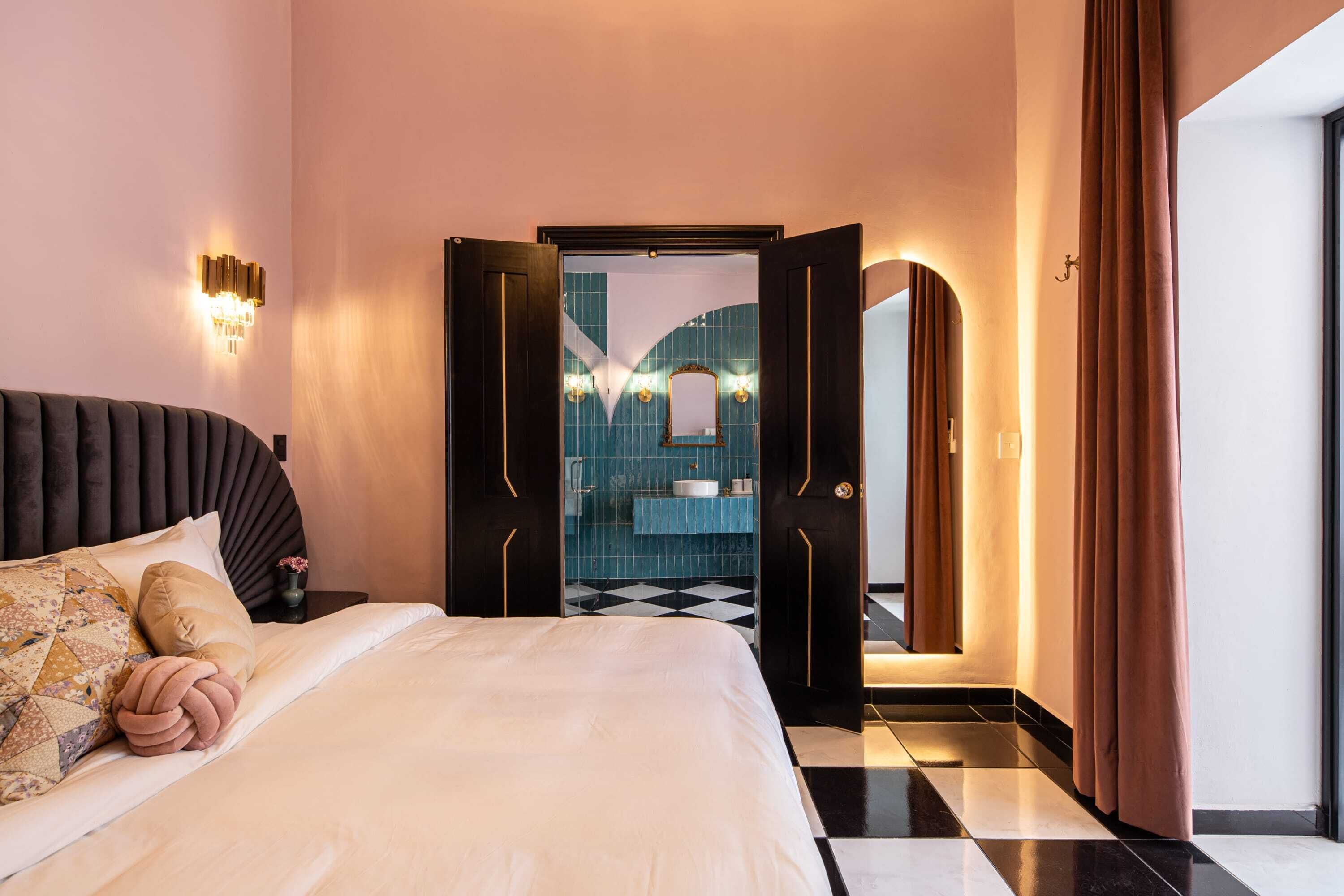 A hotel room with a bed, a nightstand, a wall-mounted light fixture, and a bathroom visible through an open door.