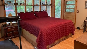 A bedroom with a large bed, wooden floor, ceiling fan, and windows with blinds.