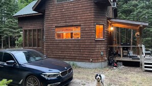 A wooden cabin with a car parked in front and a dog standing on the grass.