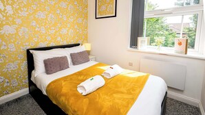 A hotel room with a bed, a window with a view, and a yellow floral wallpaper.