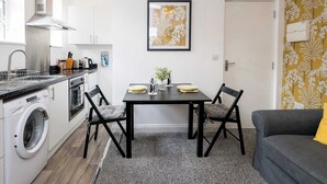 A compact kitchen with a washing machine, a dining table with chairs, and a sofa.