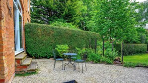 A gravel patio with a table and chairs, surrounded by a hedge and greenery.
