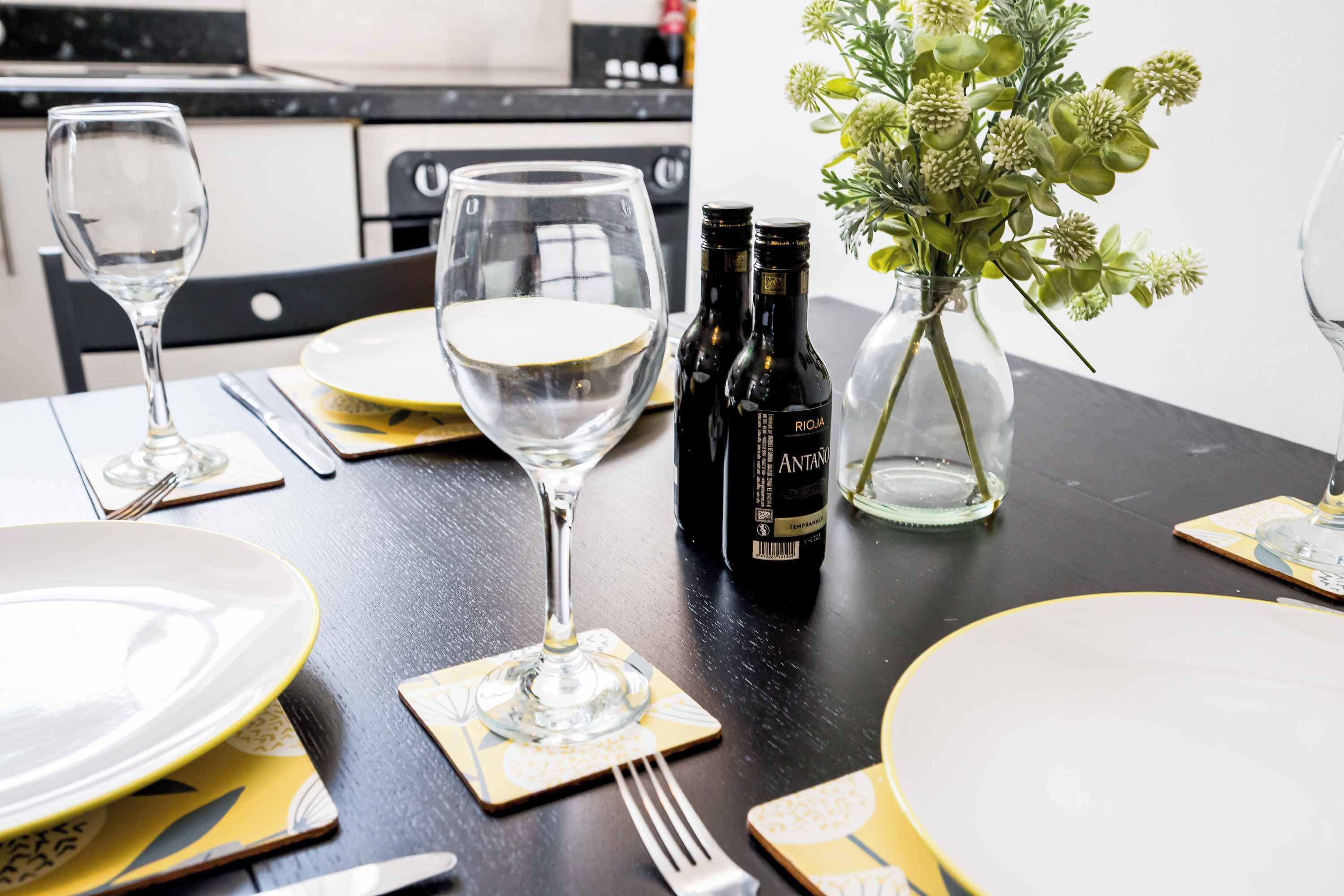 A dining table set with plates, cutlery, wine glasses, and bottles.