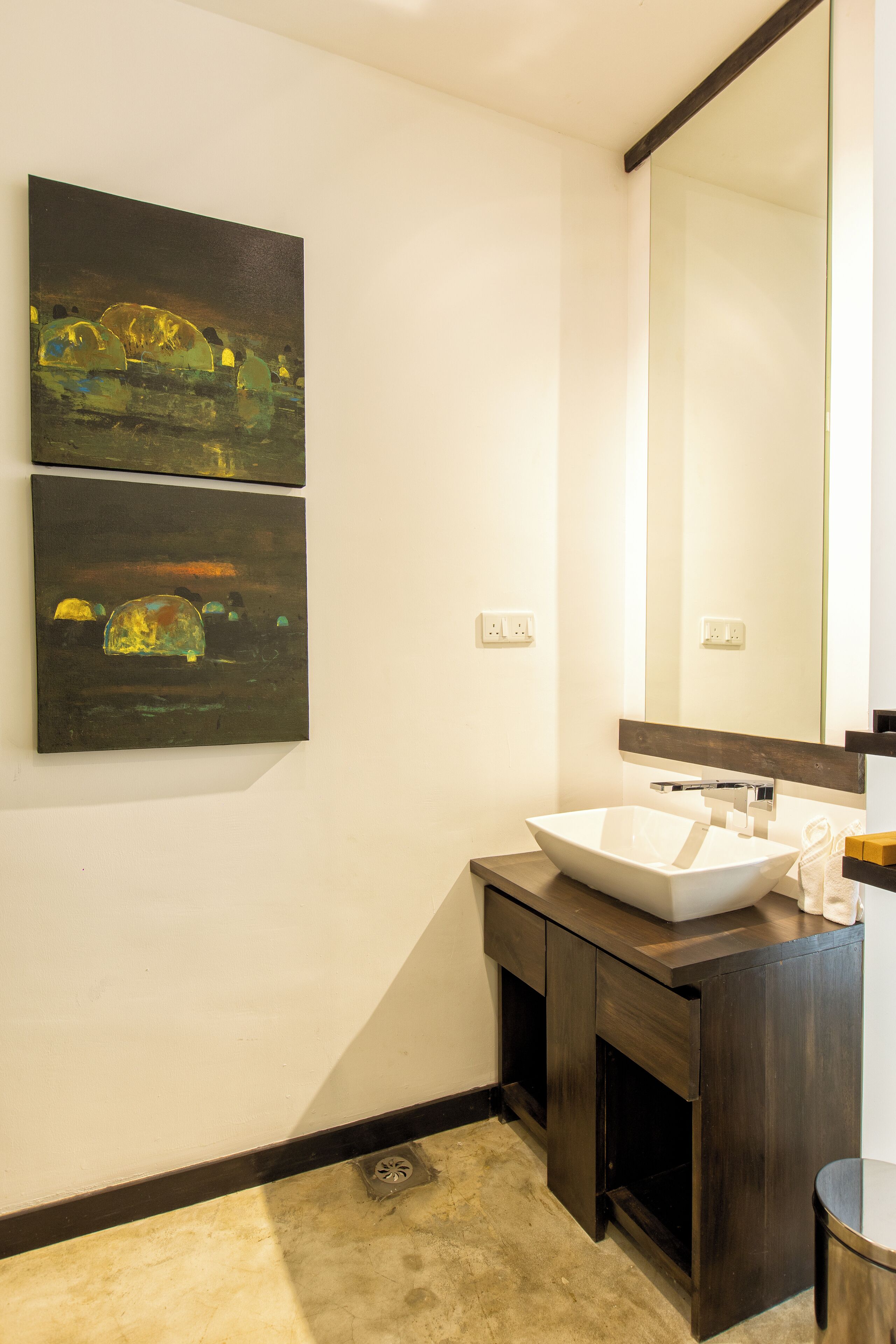 A modern bathroom with a white sink, dark wooden vanity, and two abstract paintings on the wall.