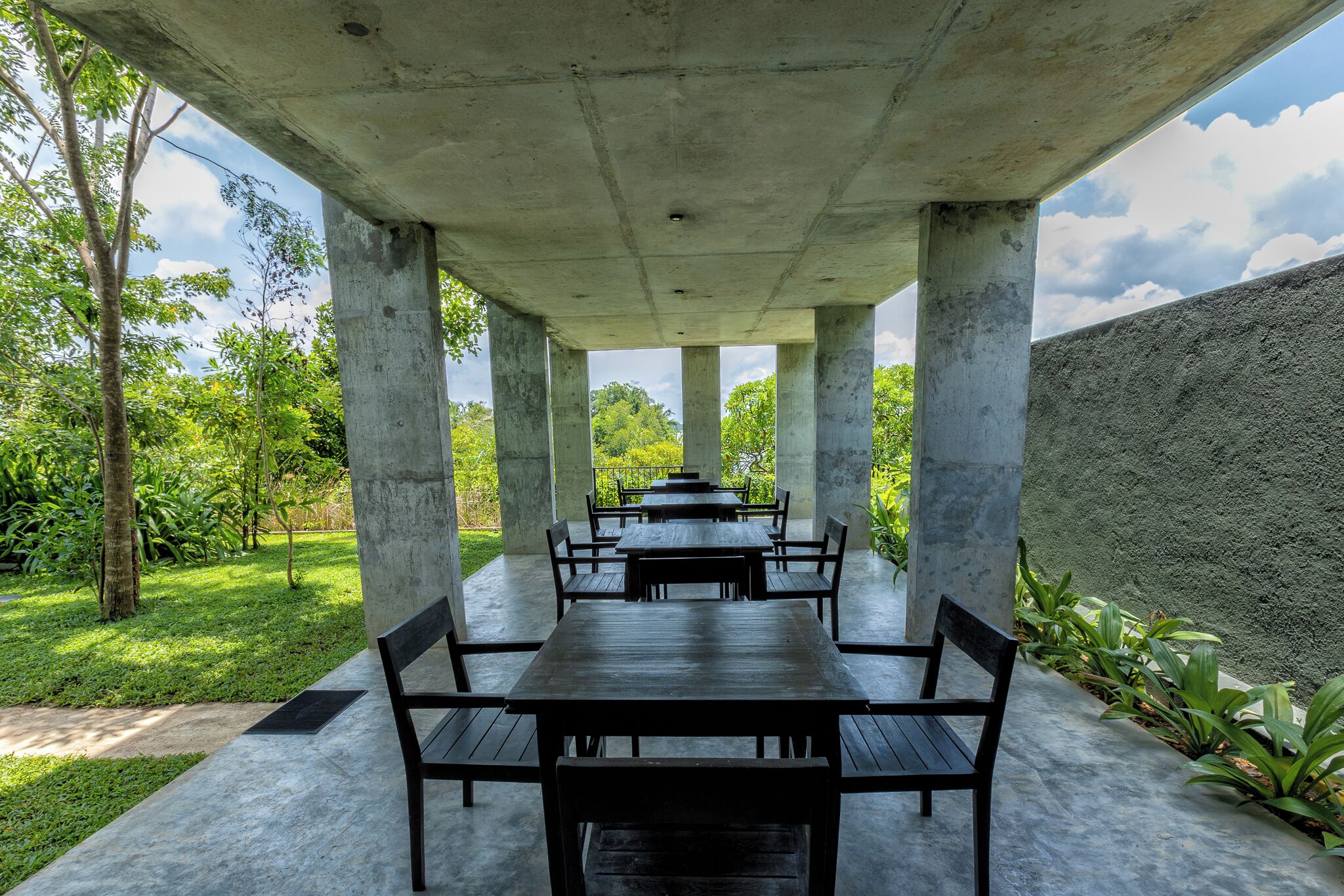 Un espace de restauration extérieur abrité, doté de piliers, de tables et de bancs en béton.