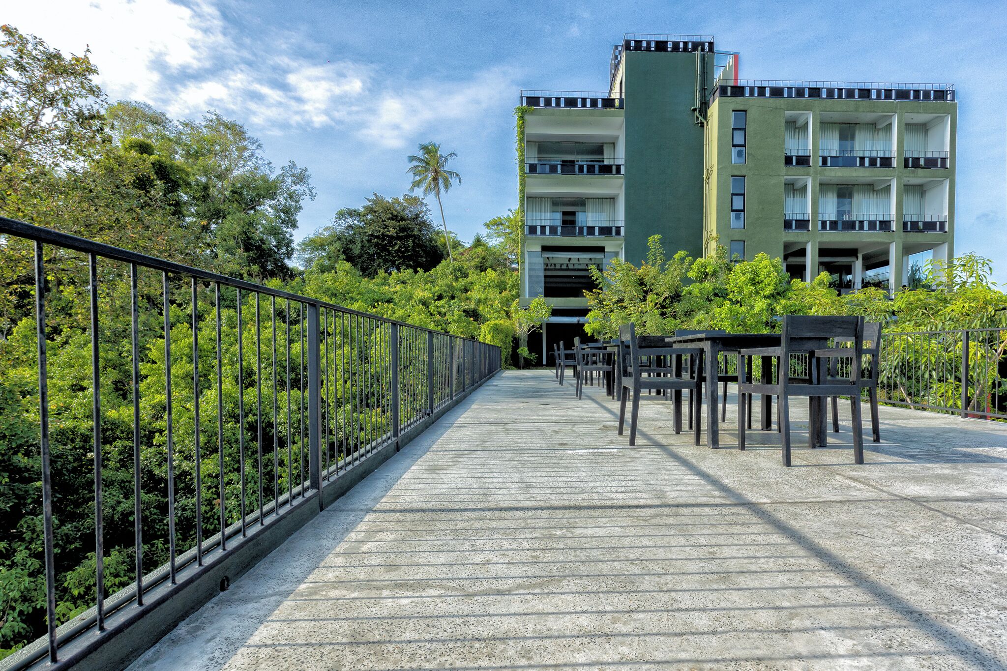 Un puente con barandilla metálica que conduce a un edificio de varios pisos con balcones y fachada verde.