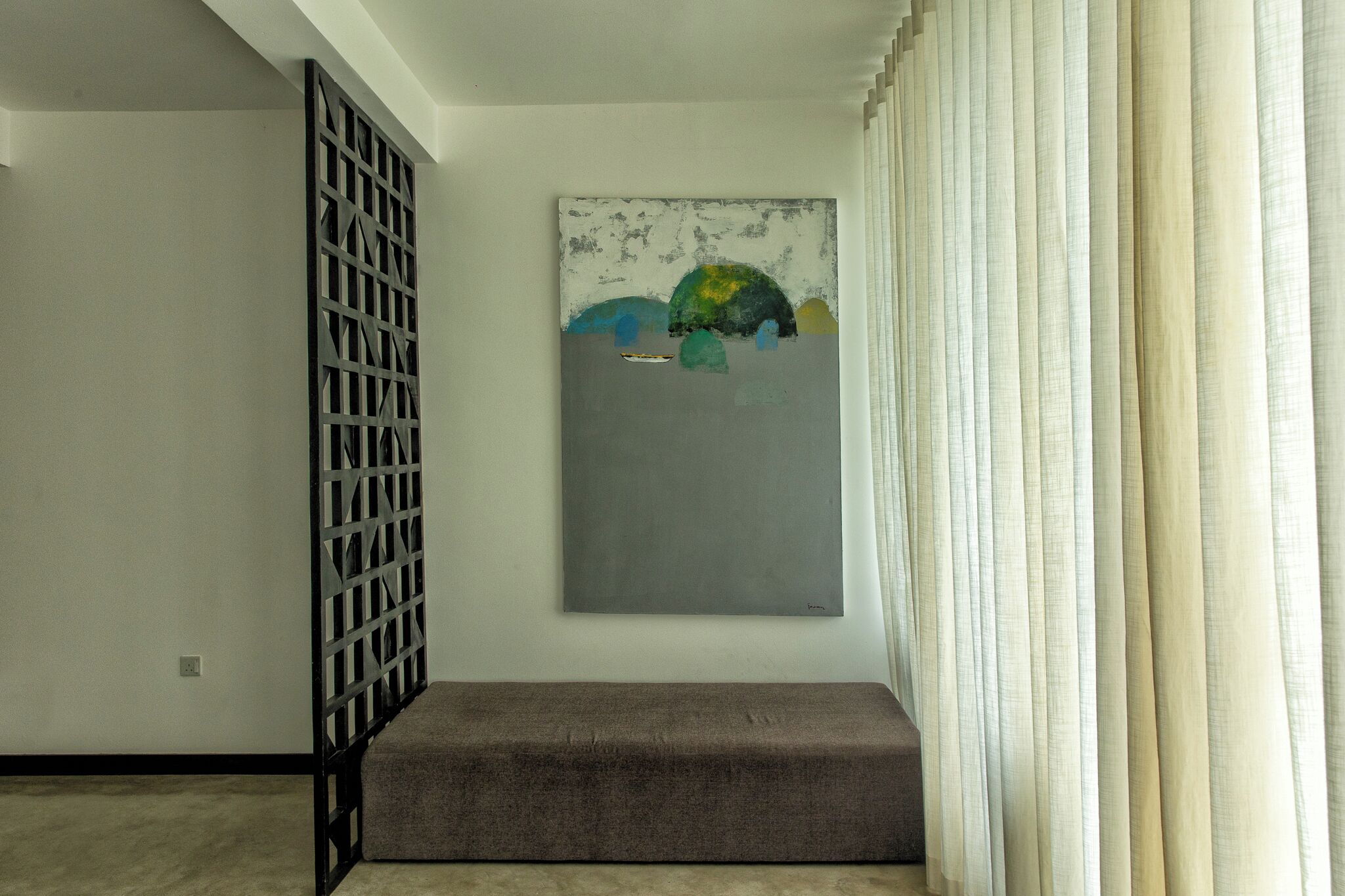 Una habitació amb un quadre abstracte gris a la paret, una partició metàl·lica negra i una banca gris.