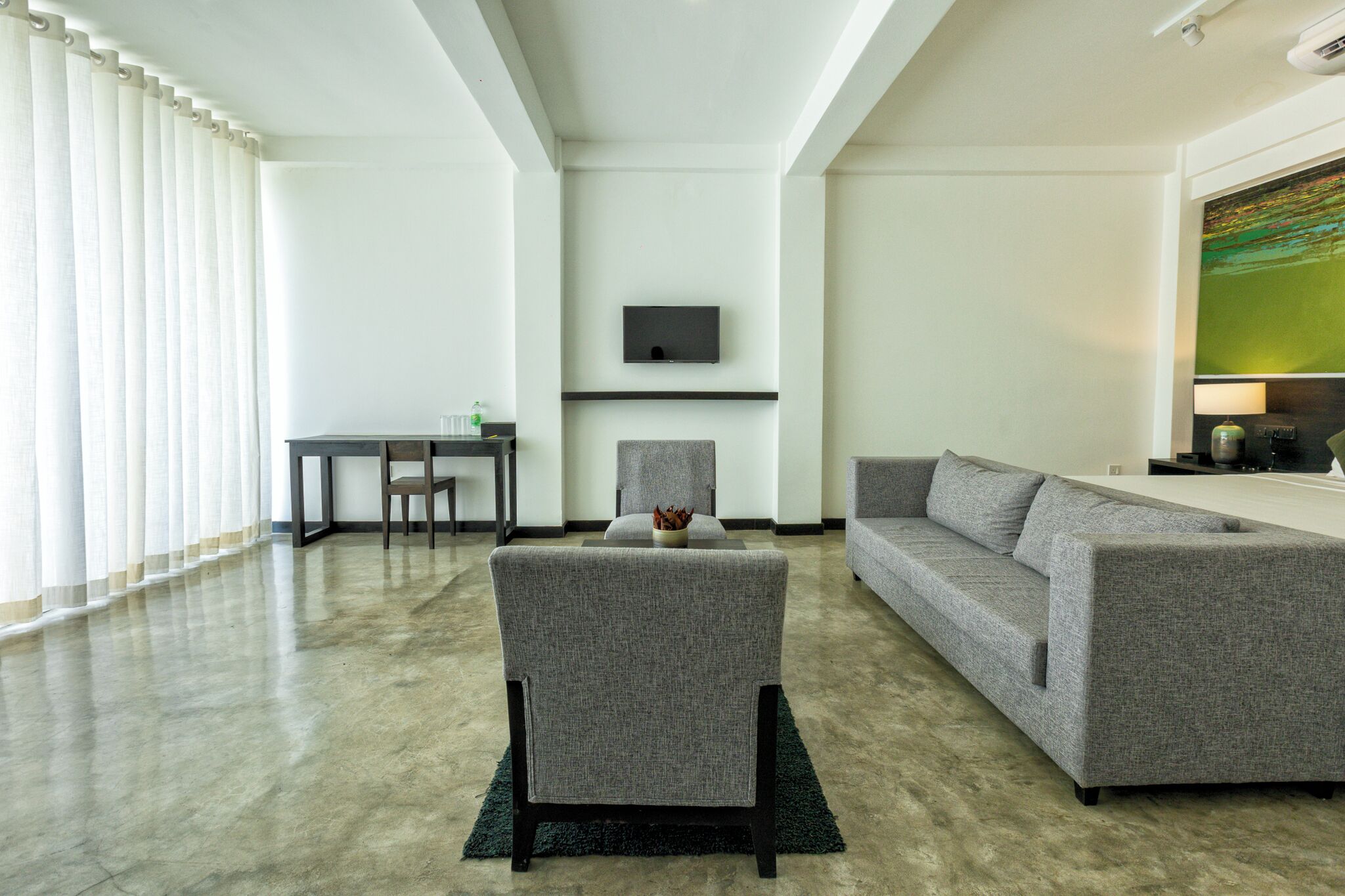 Ein modernes Wohnzimmer mit einem grauen Sofa, einem passenden Sessel, einem an der Wand befestigten Flachbildfernseher und einem Esstisch mit Stühlen.