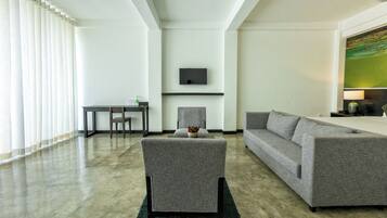 Ein modernes Wohnzimmer mit einem grauen Sofa, einem passenden Sessel, einem an der Wand befestigten Flachbildfernseher und einem Esstisch mit Stühlen.