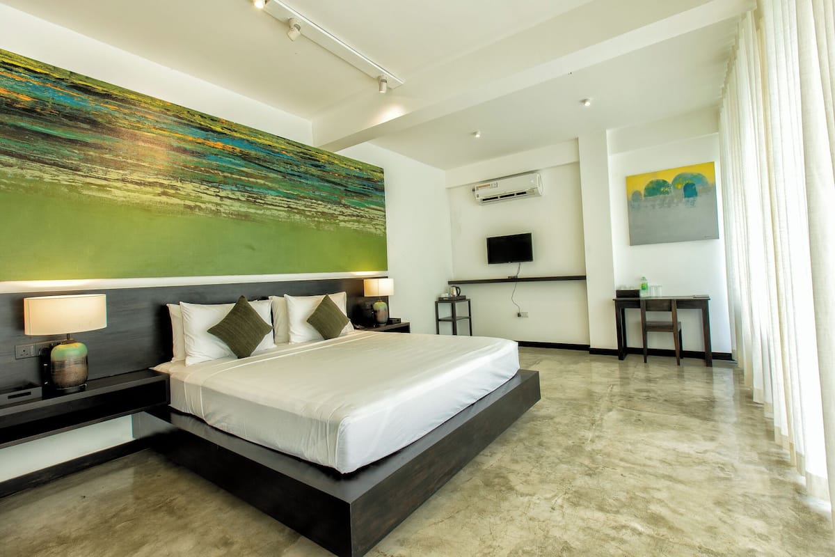 A modern hotel room with a large bed, a flat-screen TV, a desk, and a painting on the wall.