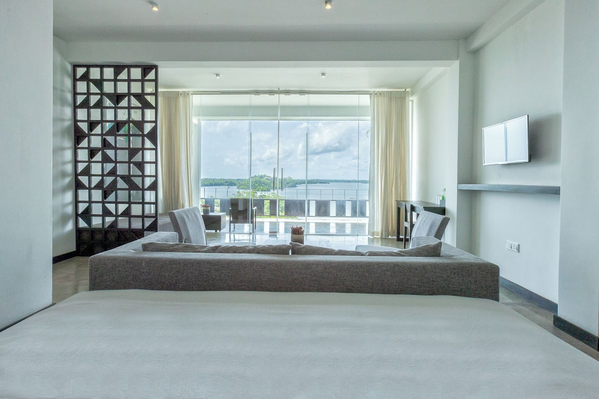 A modern hotel room with a large bed, a balcony with a view, and a TV mounted on the wall.