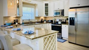 Una cocina moderna con armarios blancos, encimeras de granito, electrodomésticos de acero inoxidable e iluminación colgante.