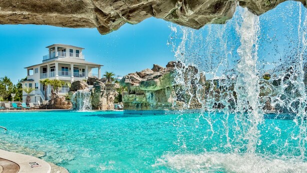 Una piscina con agua turquesa cristalina, una cascada y un edificio grande al fondo.