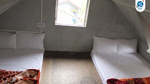 Una habitación pequeña y tenuemente iluminada con dos camas, una ventana y un enchufe a la vista.