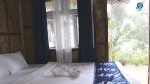 Una cama con sábanas blancas, una manta azul con el texto 'SAY' y una ventana con cortinas.