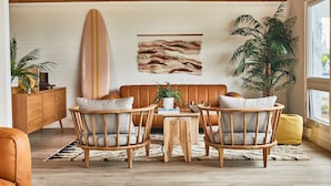 Un salón acogedor con techo de madera, una tabla de surf, una planta y un sofá con cojines.