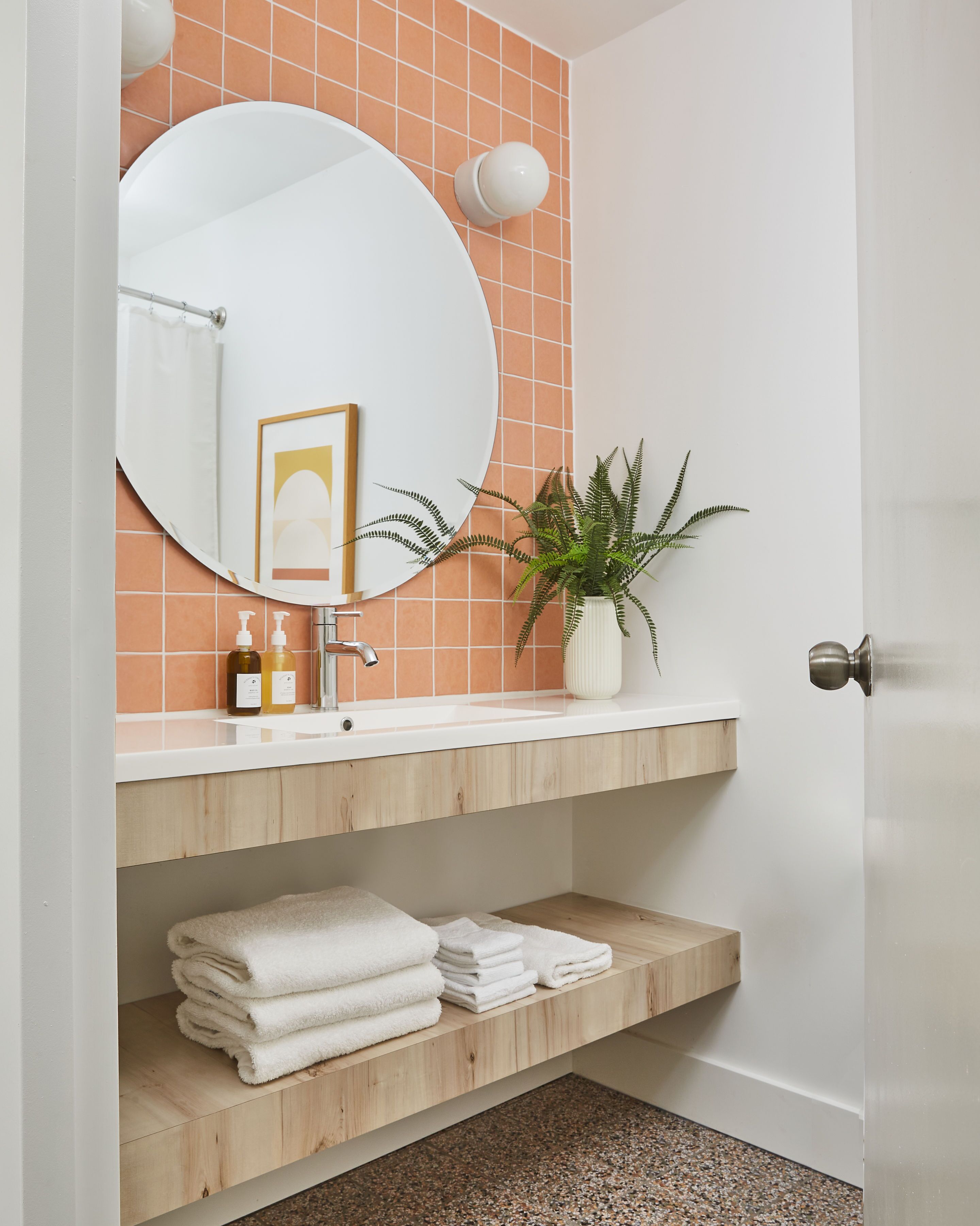 A bathroom with a white sink, a round mirror, a potted plant, and a towel rack.