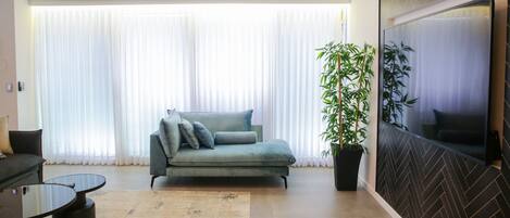 Una sala de estar moderna con un sofá, una mesa de centro, una planta grande en maceta y un televisor montado en la pared.