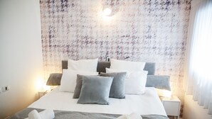A neatly made bed with multiple pillows and a blanket, a bedside lamp, and a textured wall behind. - YalaRent Midtown towers TLV (Tel Aviv)