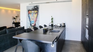 A modern kitchen with a central island, a dining area with a sofa, and a large abstract painting on the wall. - YalaRent Midtown towers TLV (Tel Aviv)