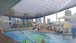A swimming pool with a wooden deck, lounge chairs, and umbrellas. - YalaRent Midtown towers TLV (Tel Aviv)