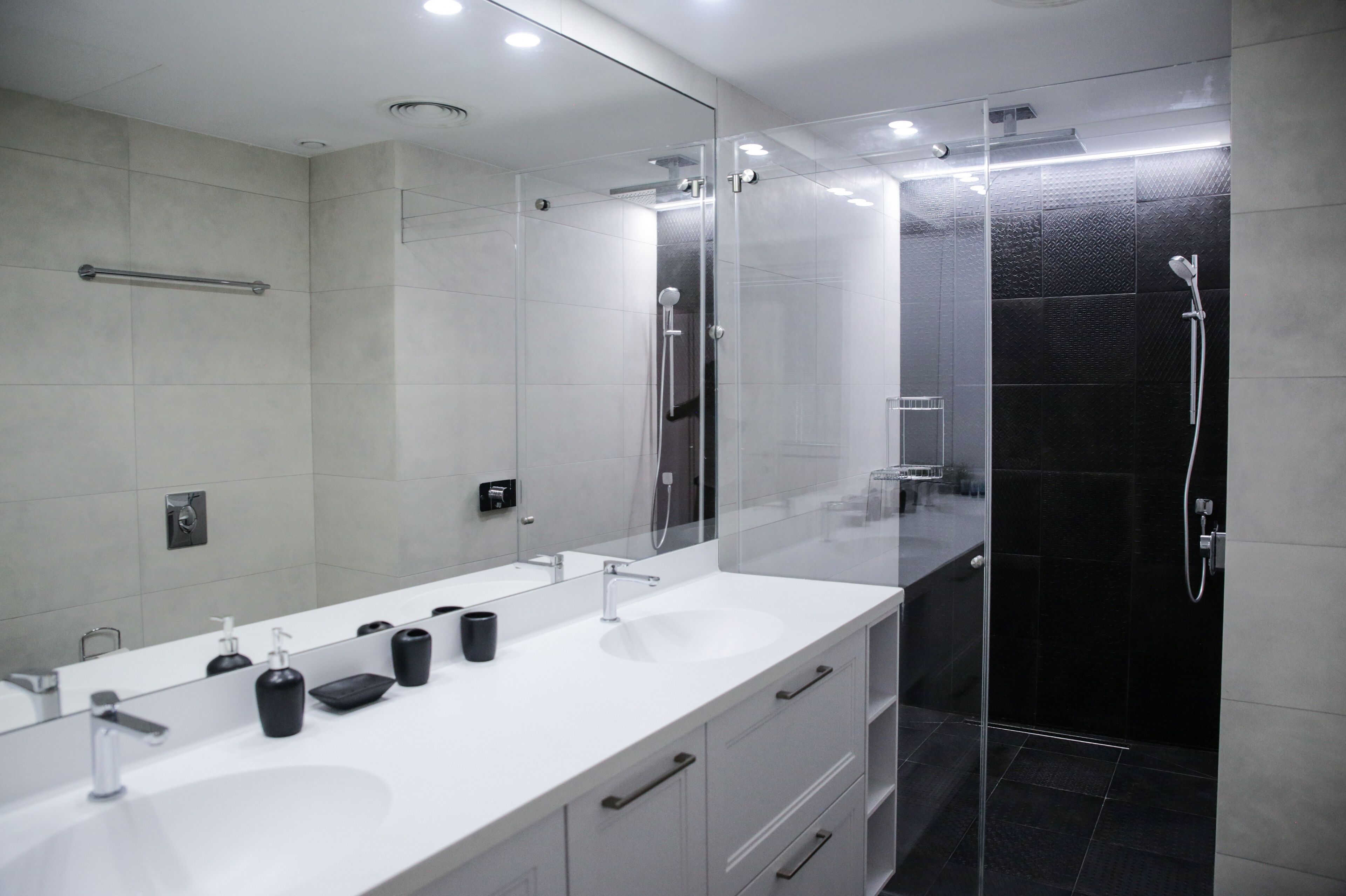 Une salle de bain moderne avec deux lavabos, un grand miroir et une douche séparée par une paroi de verre.
