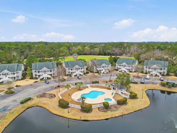 A resort with multiple two-story buildings, a central swimming pool, and a surrounding water body.