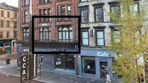 Une vue de rue avec un immeuble doté de nombreuses fenêtres et d’une devanture portant l’inscription « iCafe ».