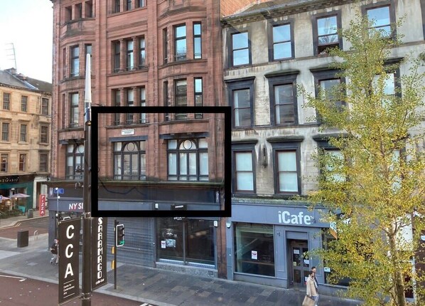 Une vue de rue avec un immeuble doté de nombreuses fenêtres et d’une devanture portant l’inscription « iCafe ».